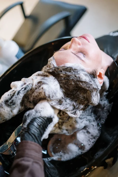 Eingeschäumtes Haar wird am Salonwaschbecken mit behandschuhten Händen gewaschen