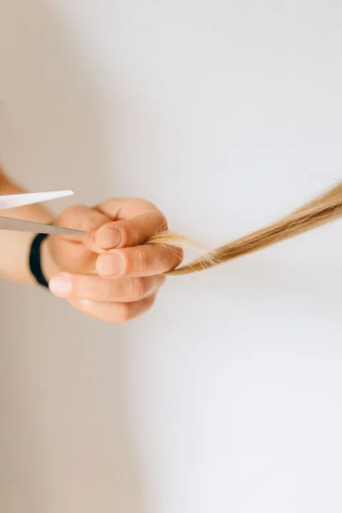 Hand hält eine Haarsträhne zwischen den Fingern neben einer Schere