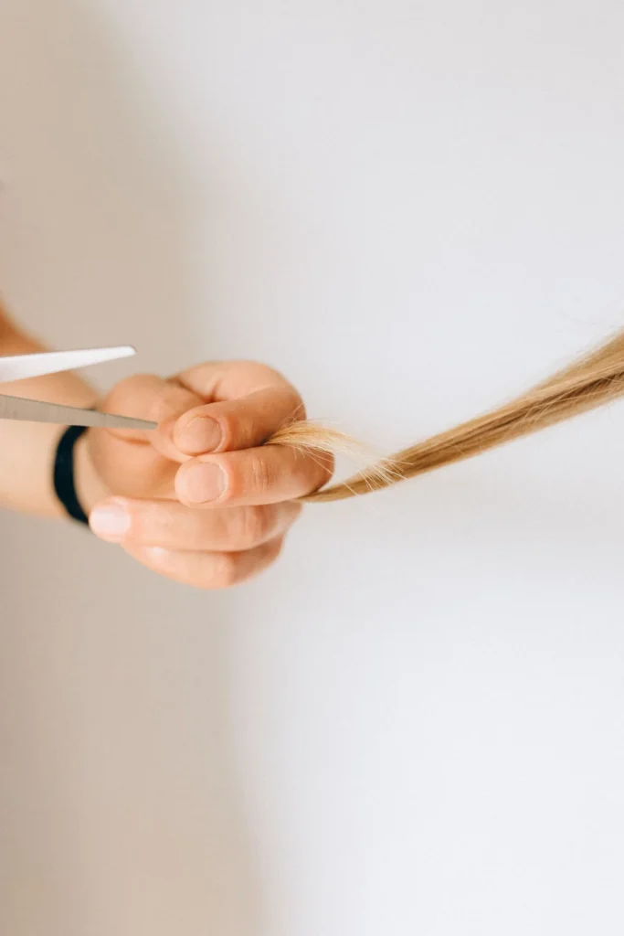 Hand hält eine Haarsträhne zwischen den Fingern neben einer Schere
