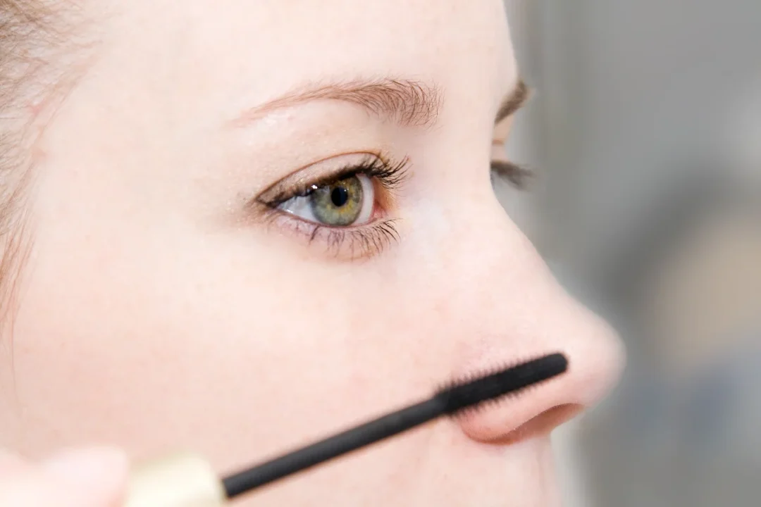 Mascara-Bürstchen vor dem Gesicht und bereits geschminkte Wimpern