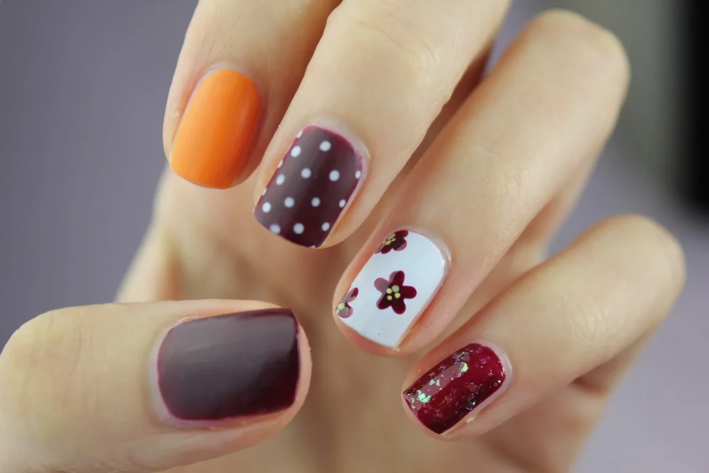 Fingernägel mit orangefarbenem Lack, Punkten und Blumenmotiven