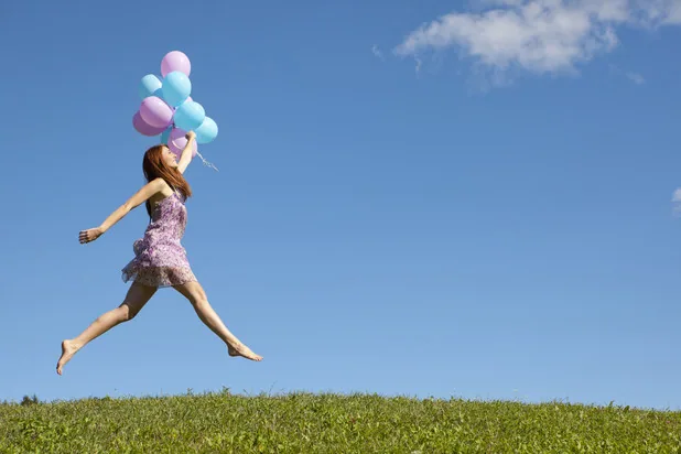 Frau springt auf einer Wiese mit Luftballons