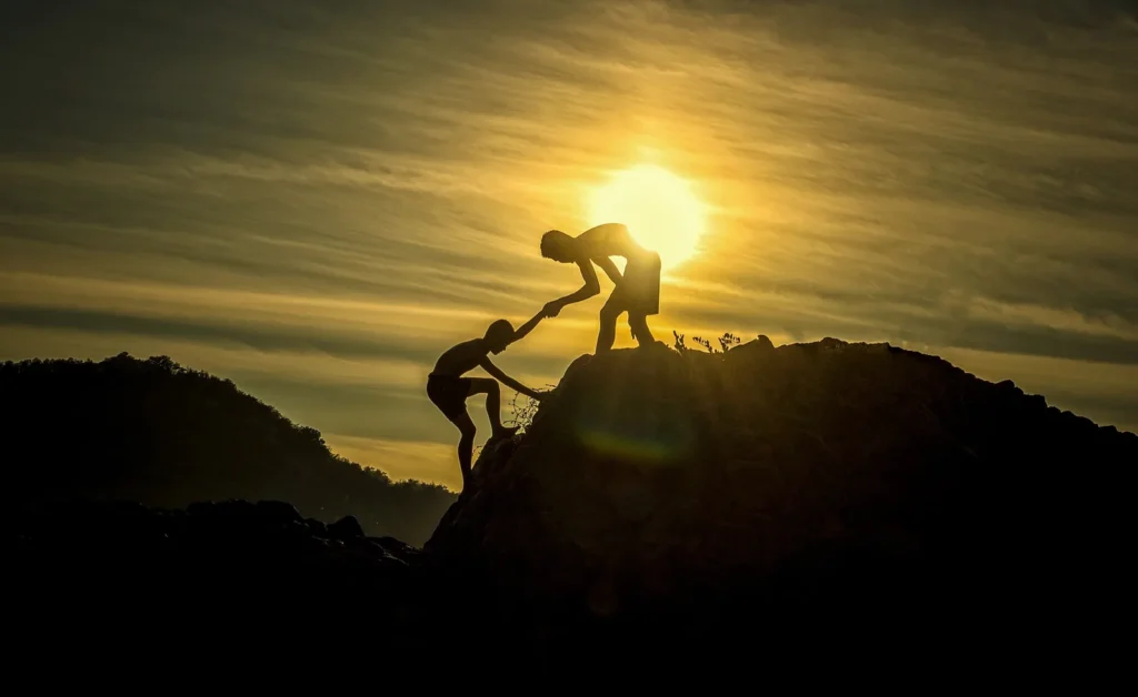 Zwei Menschen helfen einander auf einen Felsen im Sonnenuntergang