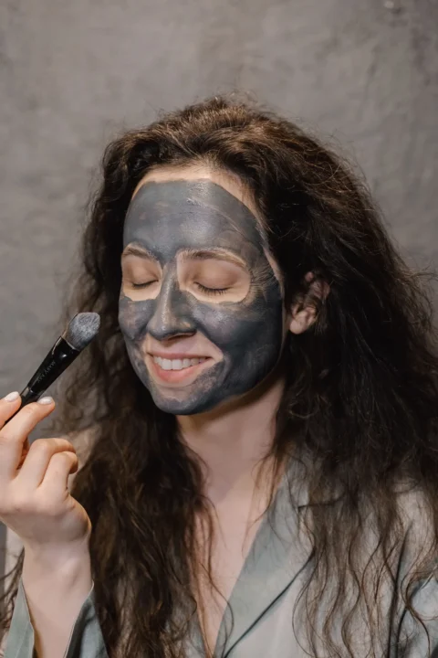 Frau trägt mit einem Pinsel eine graue Gesichtsmaske auf